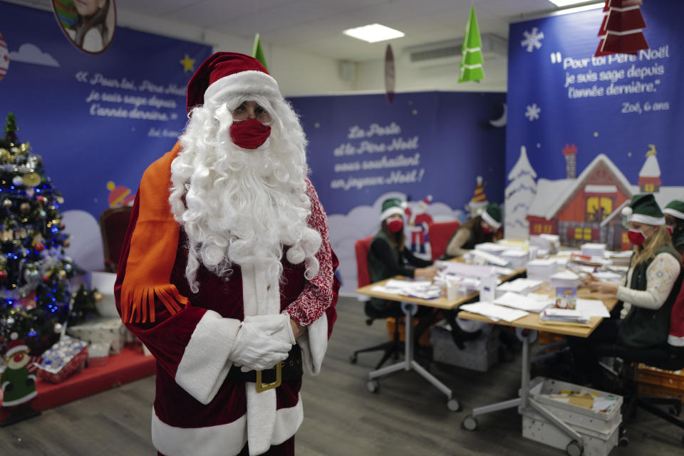 A postal worker dressed as Santa, talks with co-workers who call themselves "Elves" as they open envelopes addressed to "Pere Noel" - Father Christmas in French - decorated with love hearts, stickers and glitter, in Libourne, southwest France, Monday, Nov. 23, 2020. Letters pouring by the tens of thousands into Santa's mailbox offer a glimpse into the worries and hopes of children awaiting a pandemic-hit Christmas. Along with usual pleas for toys and gadgets, kids are also mailing requests for vaccines, for visits from grandparents, for life to return to the way it was. The office estimates that one letter in three mentions the pandemic. (AP Photo/Francois Mori)