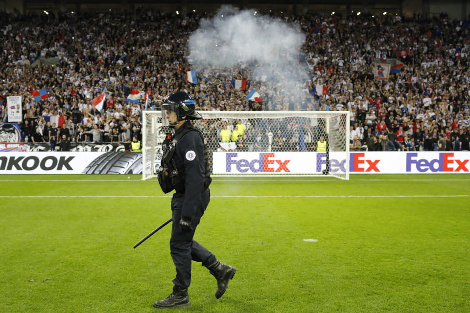 Un agente policial camina por la cancha, invadida por varios hinchas, unos minutos antes de la hora en que debía comenzar el partido entre el local Lyon y Besiktas, correspondiente a los cuartos de final de la Liga Europa, el jueves 13 de abril de 2017 (AP Foto/Laurent Cipriani)
