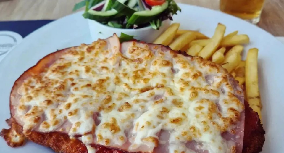 Cheap chicken parmigiana on a plate of chips and salad with a schooner of beer nearby