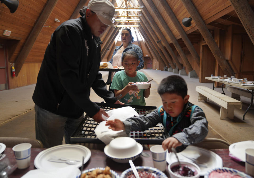 Alanna Harvey, 7, center, and other family members, set the table before a ceremonial meal at the Celilo Village Longhouse on Sunday, June 19, 2022, in Celilo Village, Ore. The tribe's first foods are placed on the table in seasonal order. (AP Photo/Jessie Wardarski)