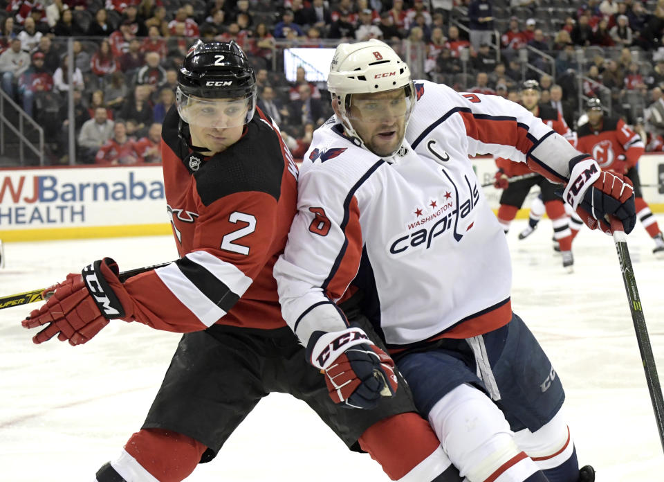 Washington Capitals left wing Alex Ovechkin (8) and New Jersey Devils defenseman Colton White (2) chase after the puck during the first period of an NHL hockey game Saturday, Feb. 22, 2020, in Newark, N.J. (AP Photo/Bill Kostroun)
