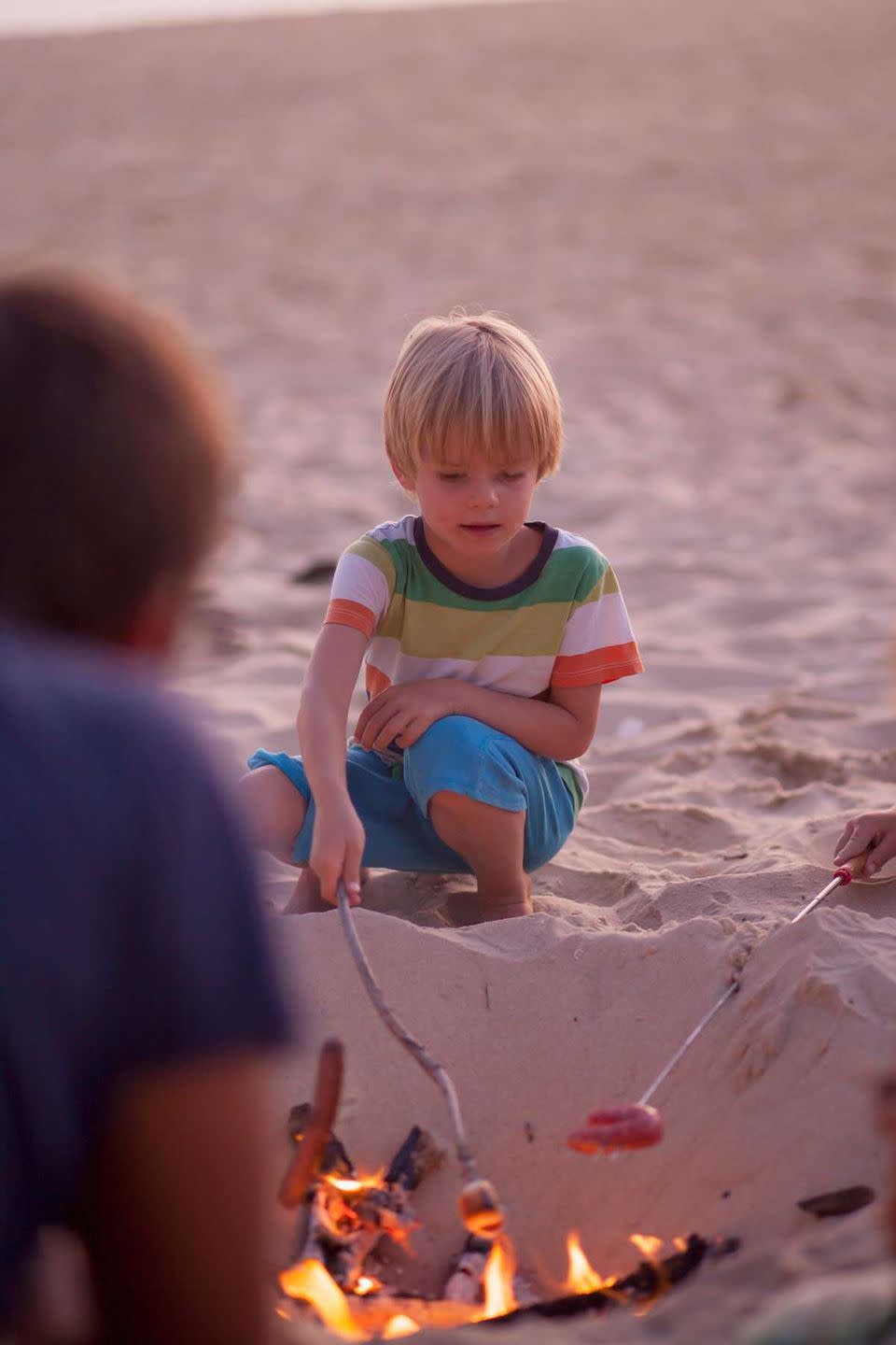 summer activities boy roast a hot dog by a bonfire on a beach