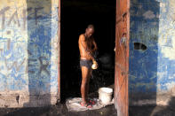 In this Dec. 3, 2019 photo, Odolph Jeudy, a charcoal seller, bathes, framed in the entrance of his shop in the Cite Soleil slum of Port-au-Prince, Haiti. When the new round of protests began in mid-Sept., Haiti's economy was already fragile, but the protests also squeezed incomes, shuttered businesses and disrupted the transportation of basic goods like charcoal, the main source of energy in the country. (AP Photo/Dieu Nalio Chery)