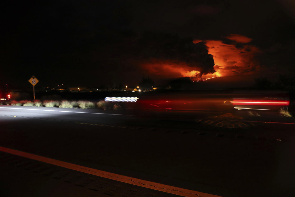As the Mauna Loa eruption takes place in the background, a car travels down Saddle Road, Tuesday, Nov. 29, 2022, near Hilo, Hawaii. Despite local authorities enforcing a no parking zone in the area near the eruption site, many spectators are flooding the area and illegally parking on the side of the highway. (AP Photo/Marco Garcia)