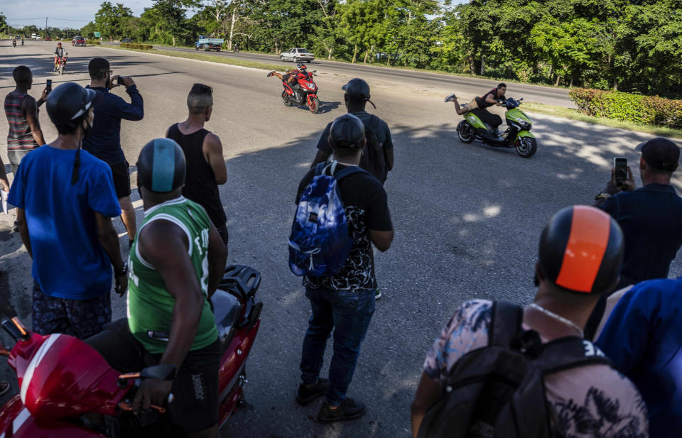 People watch a drag race between two electric scooterists at a late afternoon gathering of electric motorbike owners to show off stunts and races in Havana, Cuba, Friday, July 15, 2022. Cuba has been flooded in recent years with “motorinas”, as these electric scooters are called on the island, a fad for many, but also a solution to the transportation problems and fuel shortages that overwhelm the Caribbean nation. (AP Photo/Ramon Espinosa)