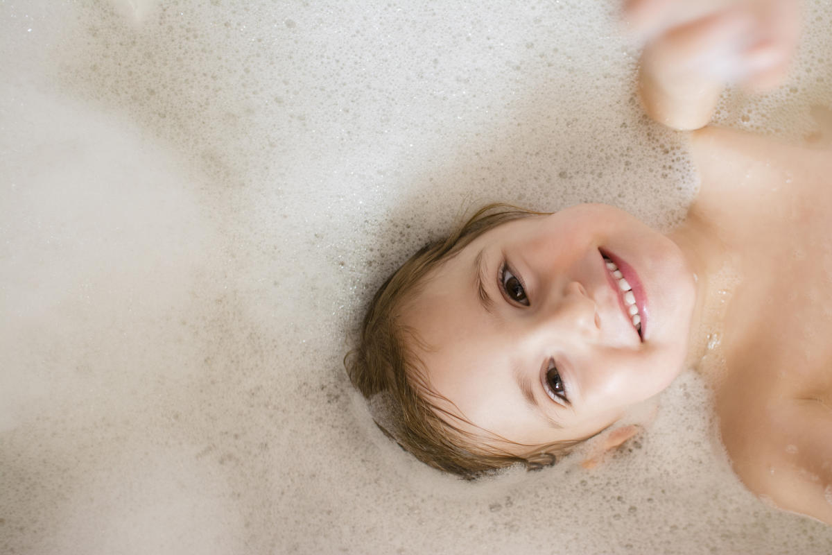 Smiling young girl bathing under a shower at home. Beautiful teen