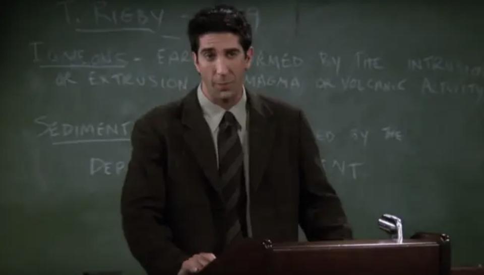 Ross wearing a suit and standing in front of a blackboard