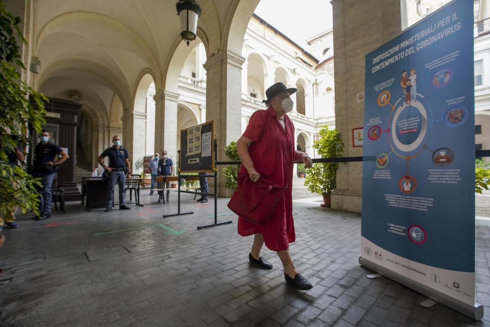 A woman walks past a poster showing how to avoid the spreading of COVID-19 as she arrives to vote at a polling station, in Rome, Sunday, Sept. 20, 2020. On Sunday and Monday Italians are called to vote nationwide in a referendum to confirm a historical change to the country's constitution to drastically reduce the number of Members of Parliament from 945 to 600. Eighteen million of Italian citizens will also vote on Sunday and Monday to renew local governors in seven regions, along with mayors in approximately 1,000 cities. (AP Photo/Andrew Medichini)