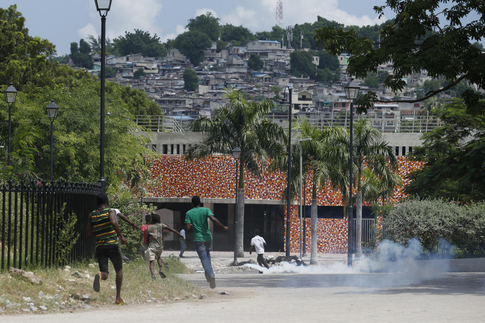 Protesters and kids run from tear gas fired by police, after a handful of demonstrators set tires alight, in the Champ de Mars park adjacent to the National Palace in Port-au-Prince, Haiti, Monday, Oct. 14, 2019. Haiti's embattled president faced a fifth week of protests on Monday as road blocks went up across the country after opposition leaders said they will not back down on their call for Jovenel Moïse to resign. (AP Photo/Rebecca Blackwell)