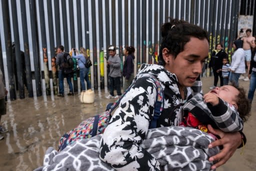 A Central American migrant carries a child after a Border Patrol sprayed them while trying to cross the US-Mexico border fence from Tijuana to San Diego, as seen from Playas de Tijuana, in Baja California state, Mexico