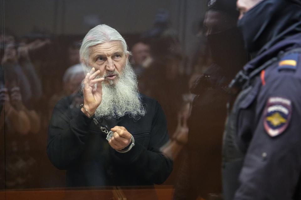 Nikolai Romanov, a former monk known as Father Sergiy until he was excommunicated by the Russian Orthodox Church, baptizes those present in the hall from behind a glass cage during his trial in Moscow, Russia, Friday, Jan. 27, 2023. The monk, who denied that the coronavirus existed and challenged the Kremlin, was handed a new prison sentence Friday on charges of inciting hatred. (AP Photo/Alexander Zemlianichenko)