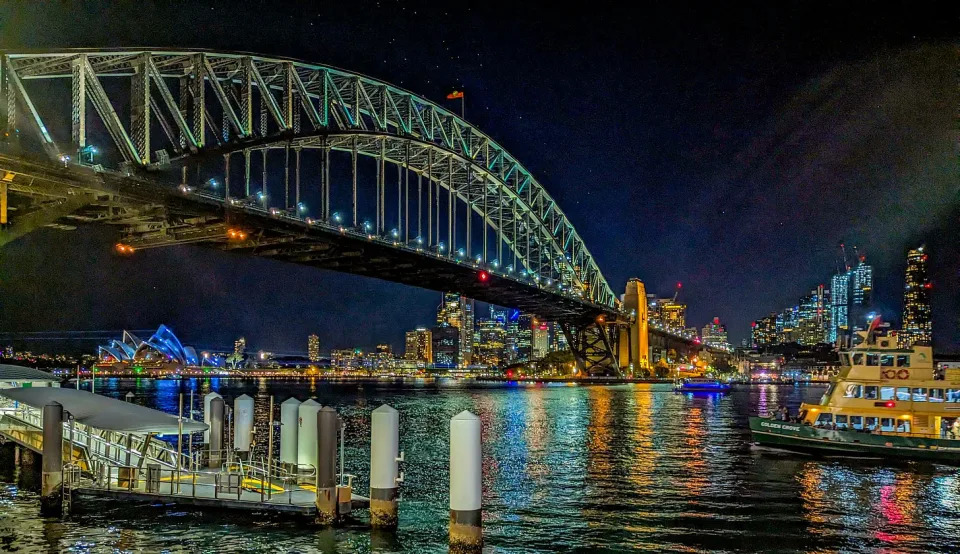 The Sydney Harbor Bridge lit up at night as a ferry approaches.