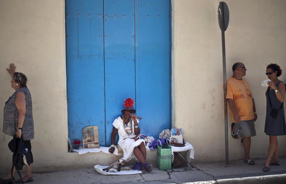 In this picture taken Sept. 11, 2012, a woman, who makes money posing for tourists, holds an oversized cigar as she waits for customers, in Havana, Cuba. When the Obama administration loosened travel restrictions to Cuba, the thought was that Americans were going to pour into the island on legal cultural exchanges. But several U.S. travel operators complain that, just over a year after the U.S. re-instituted so-called people-to-people exchanges to Cuba, applications to renew their licenses are languishing, forcing cancellations, layoffs and the loss of millions of dollars in revenue. (AP Photo/Ramon Espinosa)