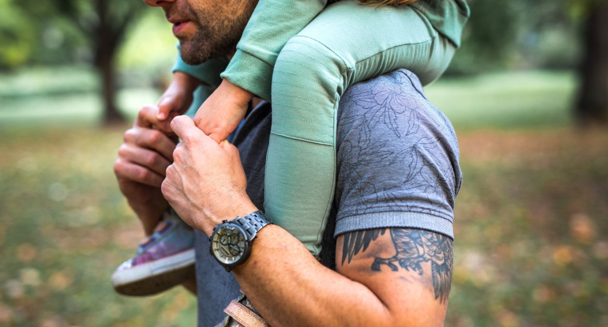 A man carries his child on his shoulder outdoors to depict Father's Day.