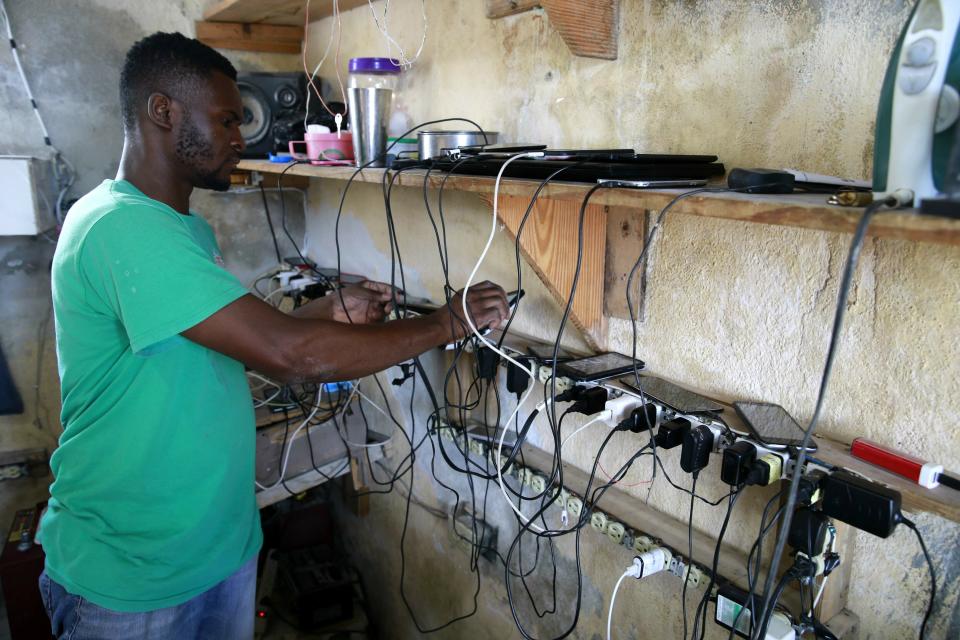 In this April 16, 2019 photo, Johny Legagneur charges phones for clients at his shop in Petion-Ville, Haiti. Johny uses an inverter and generator to charge laptops, smartphones and rechargeable bulbs for a fee. Haiti's Bureau of Monetization of Development Aid Programs, started to buy oil on the global market, but it has now said that it has run out of operating funds and stopped regularly delivering fuel needed by power station operators to keep the lights on. ( AP Photo/Dieu Nalio Chery)