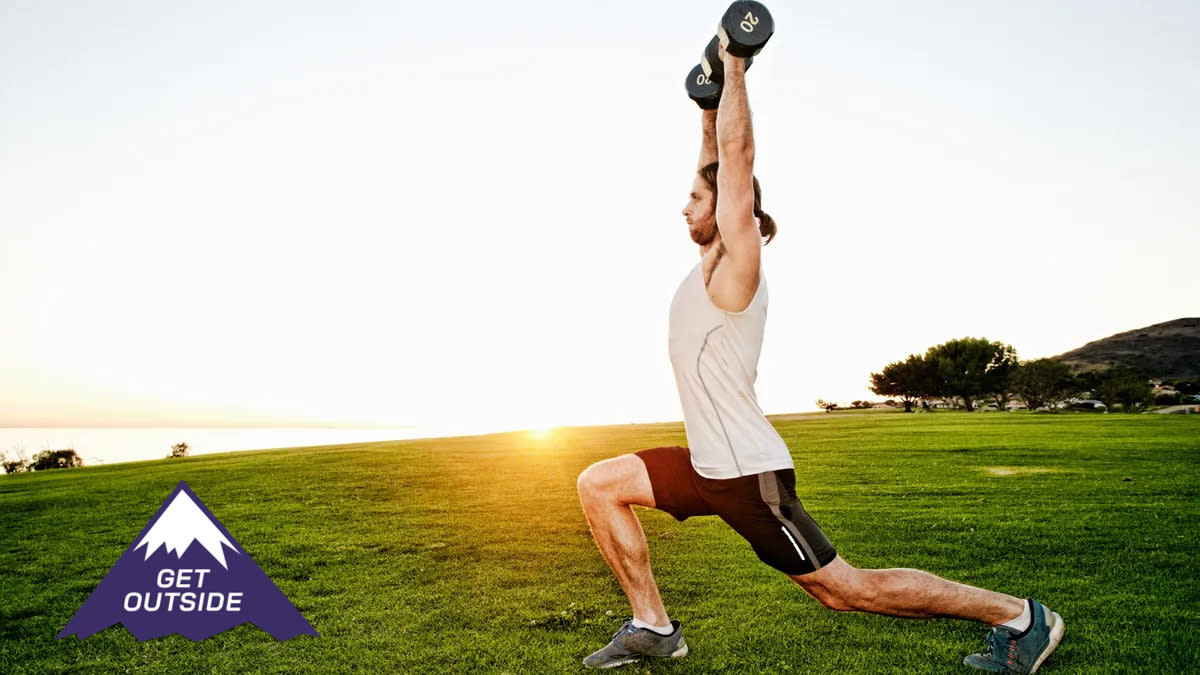  Man performing dumbbell overhead lunges on grass during outdoor workout. 