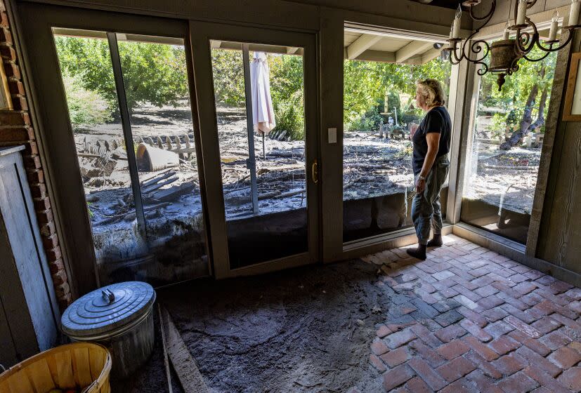 OAK GLEN, CA - SEPTEMBER 15, 2022: Resident Meg Grant stares out at mud and destruction which once was a lush patio and garden area before Monday's heavy rains breached the nearby flood channel dumping heavy mud flow and debris into her house and property on Potato Canyon Road September 15, 2022 in Oak Glen, California. Grant spent months advocating county officials to address the channel, which has flooded during other rain events. But, nothing was done. Her home and others nearby are unlivable.(Gina Ferazzi / Los Angeles Times)