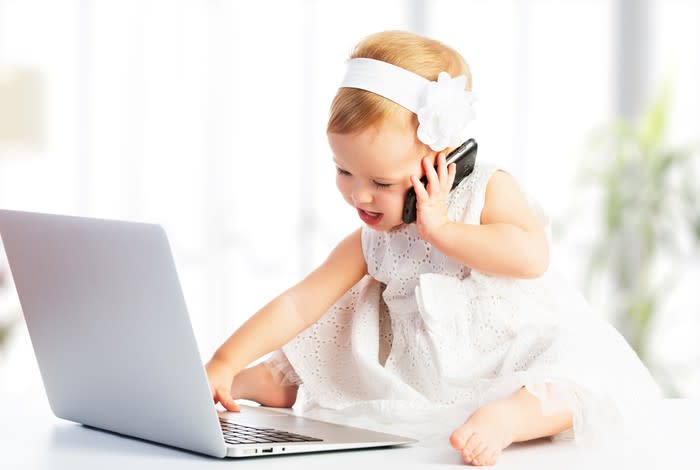 A baby holding a smartphone while playing with laptop