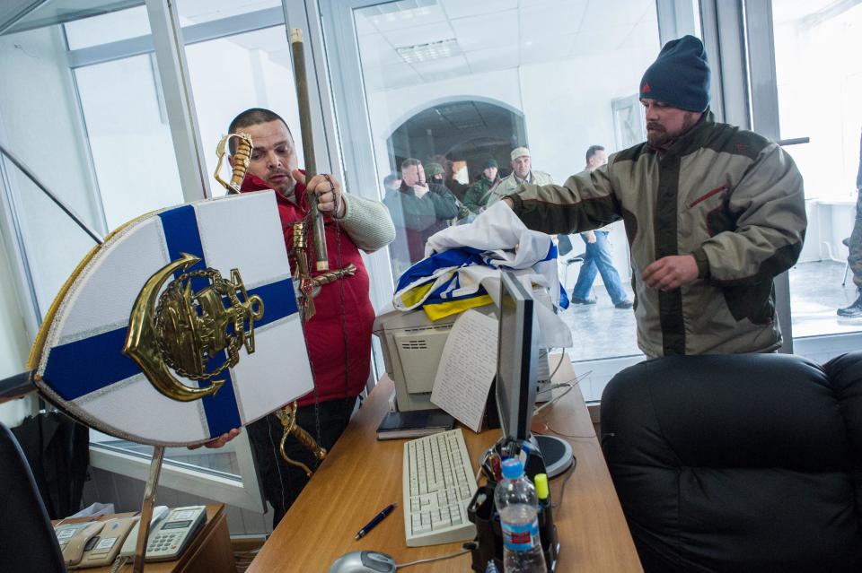 Crimean pro-Russian self-defense force members put down Ukrainian navy insignia after storming the Ukrainian navy headquarters in Sevastopol, Crimea, Wednesday, March 19, 2014. Crimea's self-defense forces on Wednesday stormed the Ukrainian navy headquarters in the Black Sea port of Sevastopol, taking possession without resistance a day after Russia signed a treaty with local authorities to annex the region. (AP Photo/Andrew Lubimov)