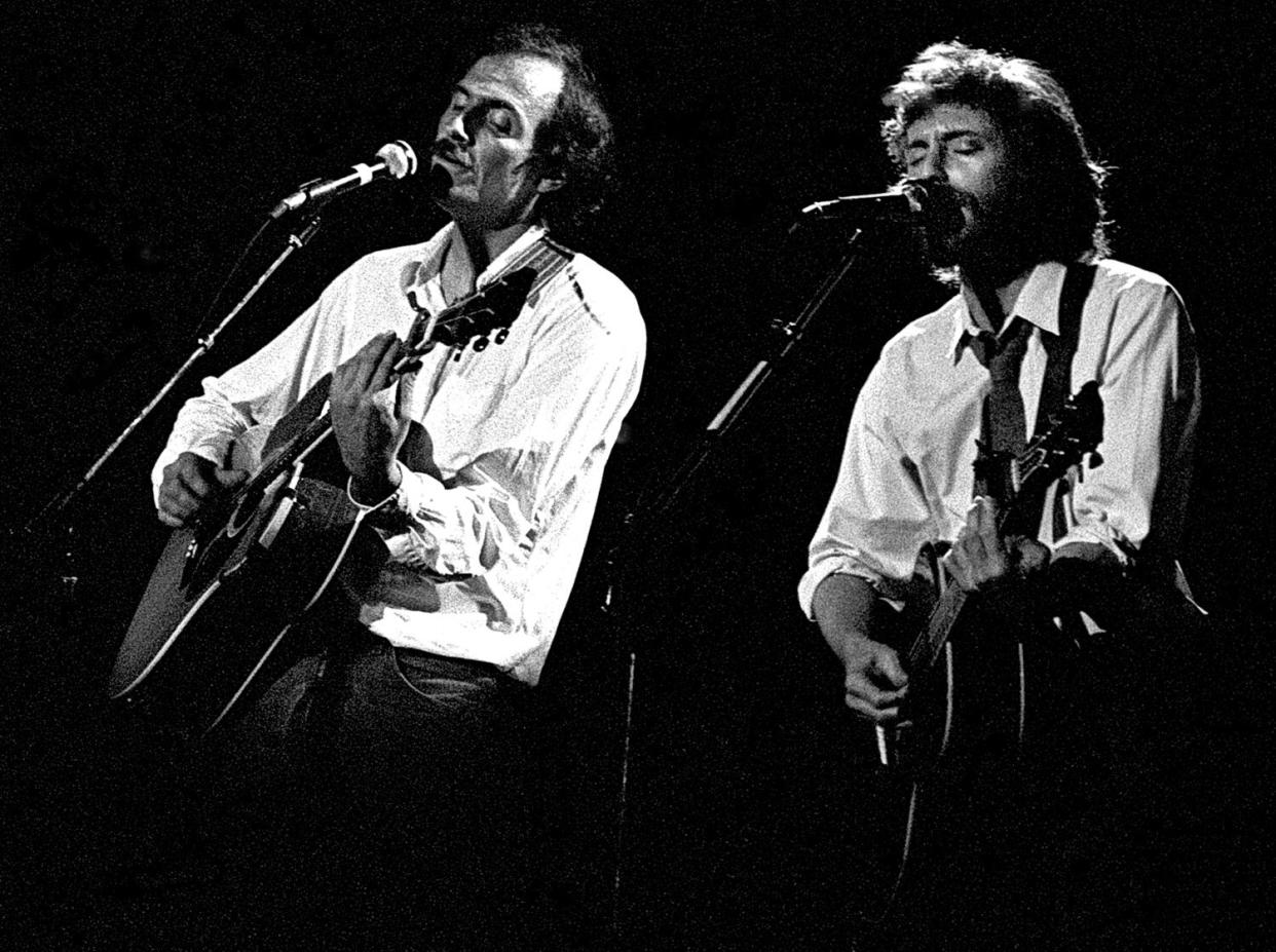 James Taylor and J.D. Souther stand singing into microphones and strumming guitars