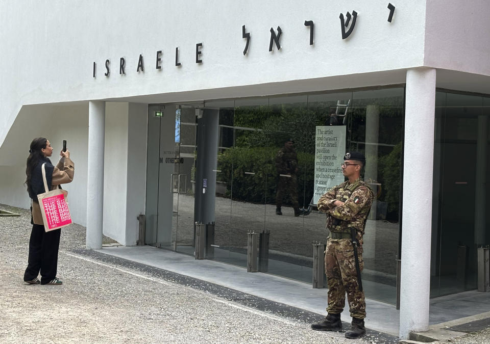 Una mujer toma una foto mientras un soldado italiano patrulla el pabellón nacional de Israel en la feria de arte contemporáneo conocida como Bienal de Venecia, en Italia, el martes 16 de abril de 2024. (AP Foto/Colleen Barry)