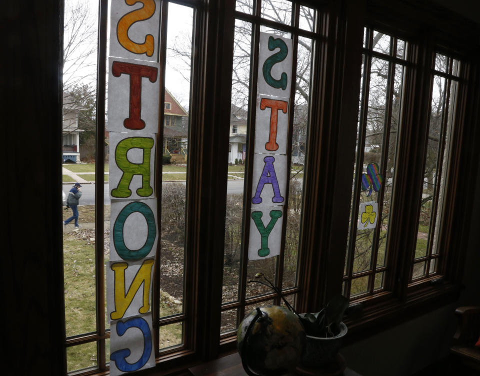 A man walks past a window in Oak Park, Ill., on Friday, March 20, 2020, before a two-week "shelter in place" order goes into effect. Leaders in the Chicago suburb were the first in the state to take the step, requiring non-essential businesses to close, to try to curb the spread of the coronavirus. (AP Photo/Martha Irvine)