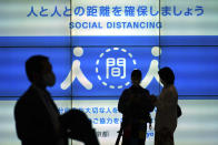 People wearing protective masks to help curb the spread of the coronavirus stand near a public awareness notice for social distancing Thursday, May 13, 2021, in Tokyo. The Japanese capital confirmed more than 1,000 new coronavirus cases on Thursday. (AP Photo/Eugene Hoshiko)