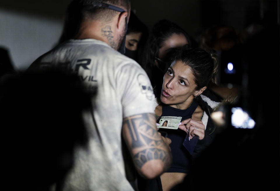 A woman presents her identification as police break up a social gathering during an operation against illegal and clandestine gatherings that authorities believe are partly responsible for fueling the spread of COVID-19, at a party hall in Sao Paulo, Brazil, early Saturday, April 17, 2021. (AP Photo/Marcelo Chello)