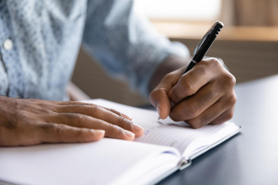 A person is writing in a notebook with a black pen. The individual's face is not visible