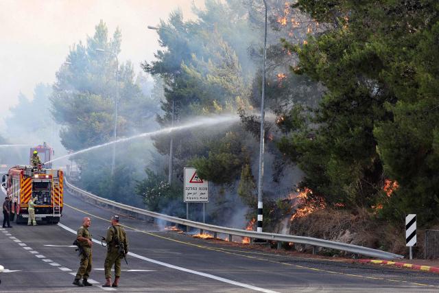 Israeli firemen spray water on trees that are burning by the side of a road