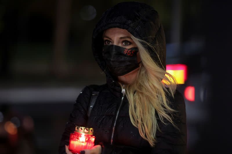 A woman holding a lit candle attends an event that commemorates the 65 victims of the Colectiv fire