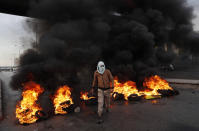 A protester passes burning tires along a main highway that leads to Beirut's international airport during a protest against the increasing prices of consumer goods and the crash of the local currency in Beirut, Lebanon, Monday, Nov. 29, 2021. (AP Photo/Hussein Malla)