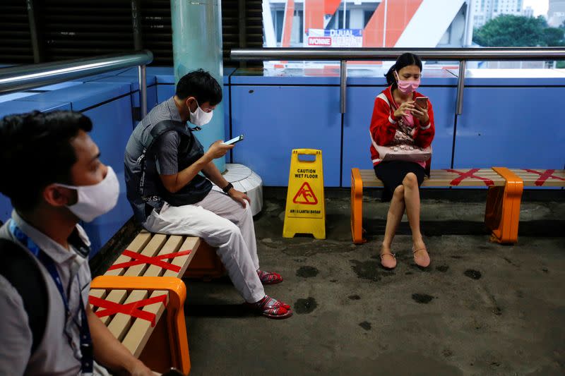 FILE PHOTO: Passengers wearing protective face masks sit on taped up benches to encourage social distancing amid the spread of coronavirus disease (COVID-19) outbreak at a train station in Jakarta