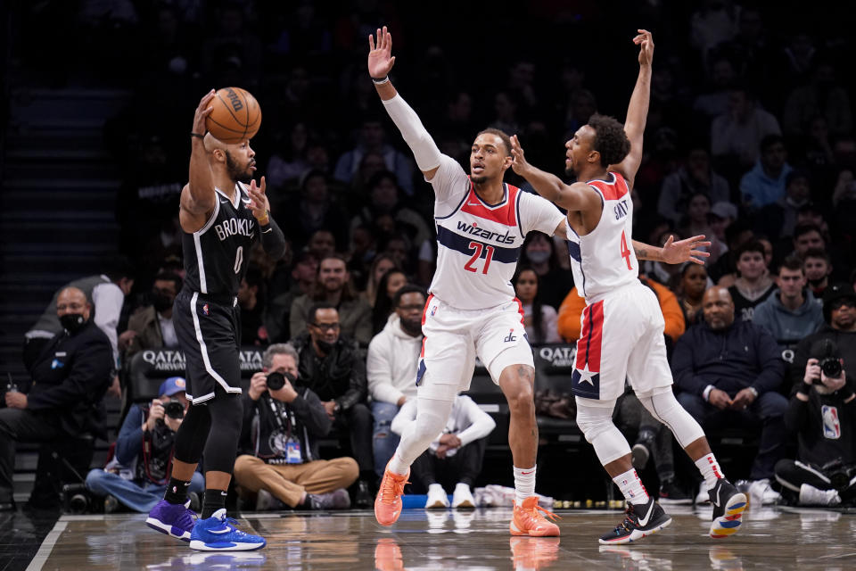 Brooklyn Nets guard Jevon Carter (0) looks to pass against Washington Wizards center Daniel Gafford (21) and guard Ish Smith (4) in the first half of an NBA basketball game, Thursday, Feb. 17, 2022, in New York. (AP Photo/John Minchillo)