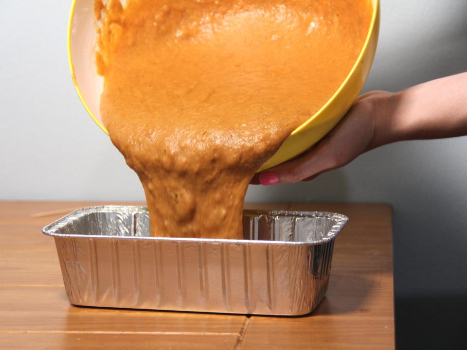 Pouring Libby's pumpkin bread mix from a bowl into a foil pan.