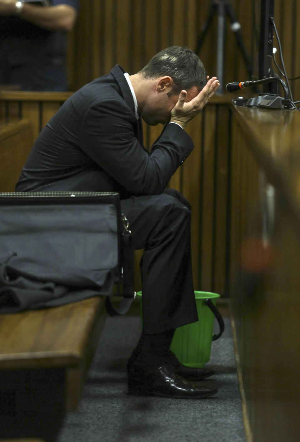 With a bucket on the floor nearby, Oscar Pistorius covers his face with his hands as he listens to cross questioning about the events surrounding the shooting death of his girlfriend Reeva Steenkamp, in court during his trial in Pretoria, South Africa, Tuesday, March 11, 2014. Pistorius is charged with the shooting death of Steenkamp, on Valentines Day in 2013. (AP Photo/Kevin Sutherland, Pool)