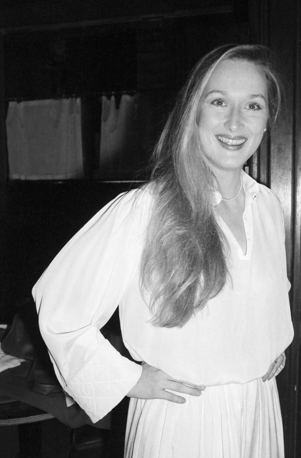 Meryl Streep smiling, wearing a long-sleeved blouse with hands on her hips