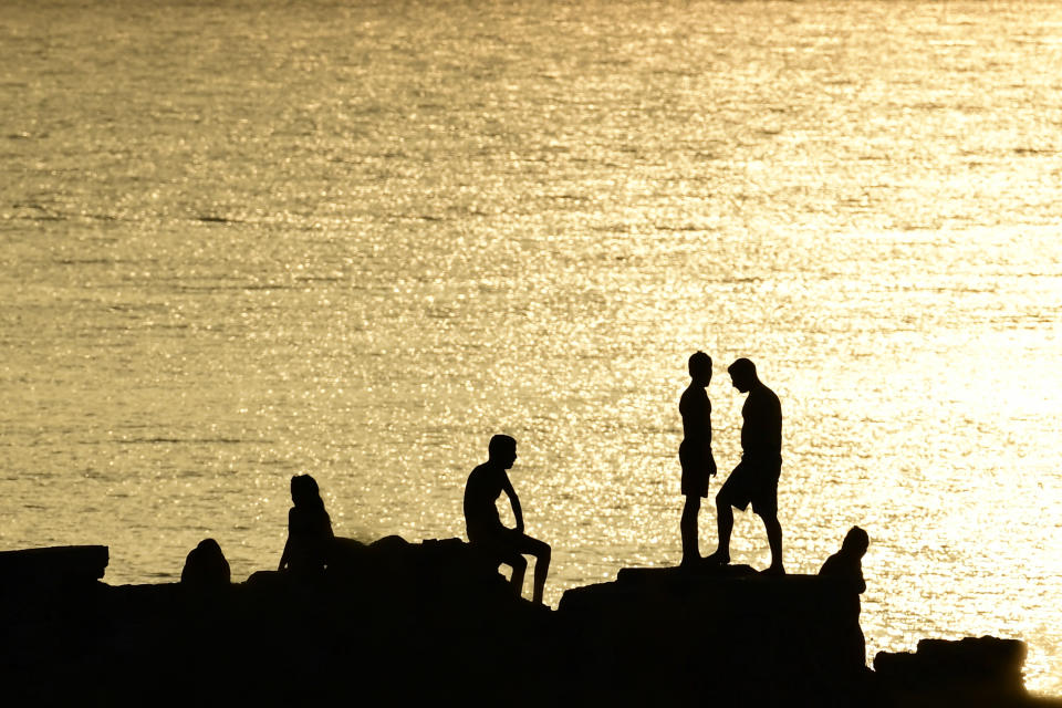 People stand on rocks near a beach of Kavouri suburb, southwest of Athens, Greece, Monday, Aug. 2, 2021. The heat wave is expected to peak Monday, with temperatures inland ranging from 42 to 46 degrees Celsius (107.6 to 114.8 Fahrenheit). Temperatures will remain at 40 Celsius (104 Fahrenheit) or above in much of Greece until at least Friday, meteorologists say. (AP Photo/Michael Varaklas)