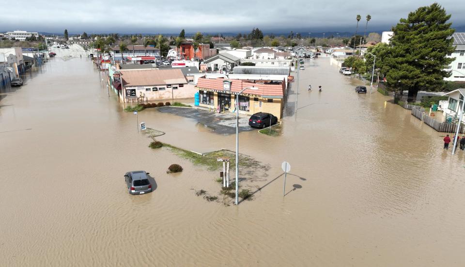 An aerial view shows people wading through a flooded neighborhood in the unincorporated community of Pajaro in Watsonville, California, on March 11, 2023. - Residents were forced to evacuate in the middle of the night after an atmospheric river surge broke the Pajaro Levee and sent flood waters flowing into the community.