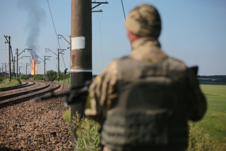 A Ukrainian serviceman stands guard by a railway line, as flames erupt in the distance from a gas pipeline damaged in shelling by pro-Russian separatists, near Avdiivka, Donetsk region, on June 12, 2015