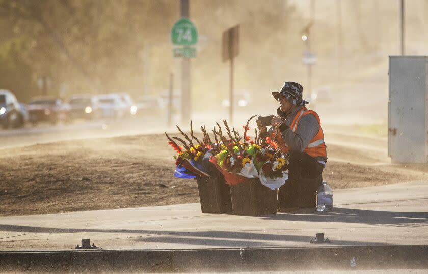 SAN JACINTO, CA - NOVEMBER 24, 2022: Juan Star uses his phone to take pictures of the powerful wind gusts blowing sand and dirt across the intersection where he is selling flowers on Thanksgiving day on November 24, 2022 in San Jacinto, California. The power is out in the area of Highway 74 and Vista Place. The San Ana winds will continue through Friday.(Gina Ferazzi / Los Angeles Times)