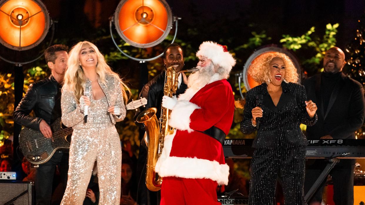  Sax-playing Santa Claus serenades pop star Cher (left), wearing glittery gold jumpsuit, on stage ahead of the iHeartRadio Jingle Ball 2023/24  . 