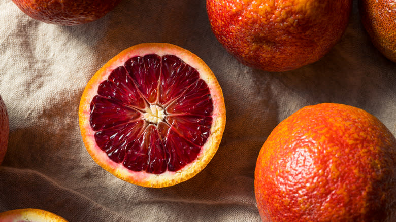 Halved and whole blood oranges on linen