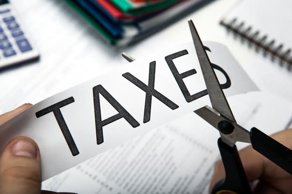 A person using scissors to cut the letter S off the word taxes.