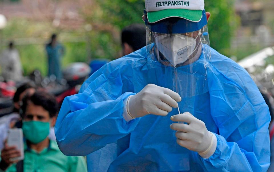 A health official wearing protective gear holds the sample of a man at a drive-through screening and testing facility for the COVID-19 coronavirus, alongside a street in Islamabad on June 10, 2020 - AFP