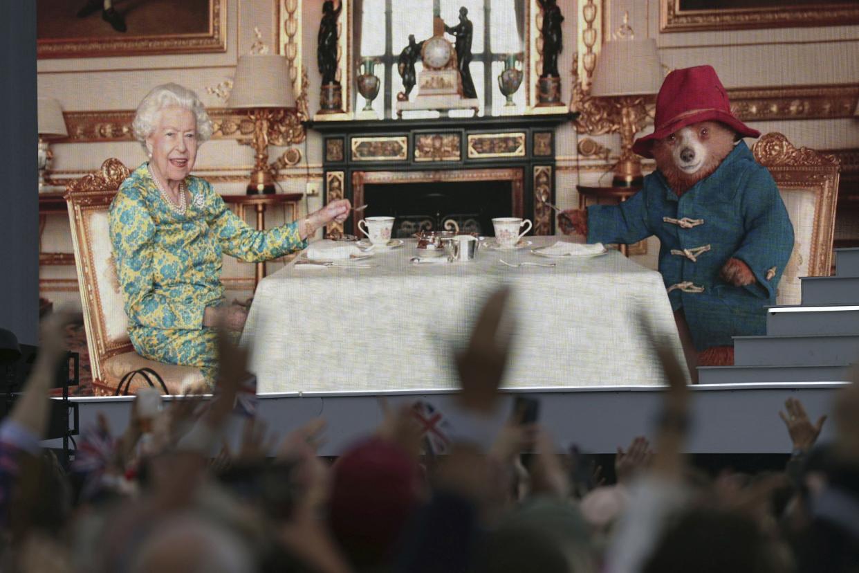 The crowd watch a film of Queen Elizabeth II having tea with Paddington Bear on a big screen at the Platinum Jubilee concert in front of Buckingham Palace in London on Saturday, June 4, 2022, on the third of four days of celebrations to mark the Platinum Jubilee.