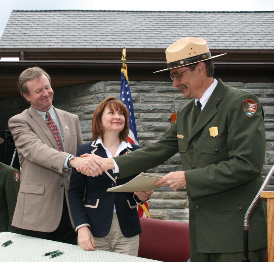 During the 2011 dedication of the new Oconaluftee Visitor Center, Terry Maddox shakes the hand of former park superintendent Dale Ditmanson, while long-time GSMA Board of Directors Chair Barbara Muhlbeier hands over signed papers transferring ownership of the building from GSMA to Great Smoky Mountains National Park.