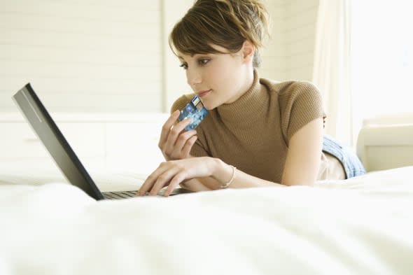 Young woman lying on bed, using laptop computer, holding credit card