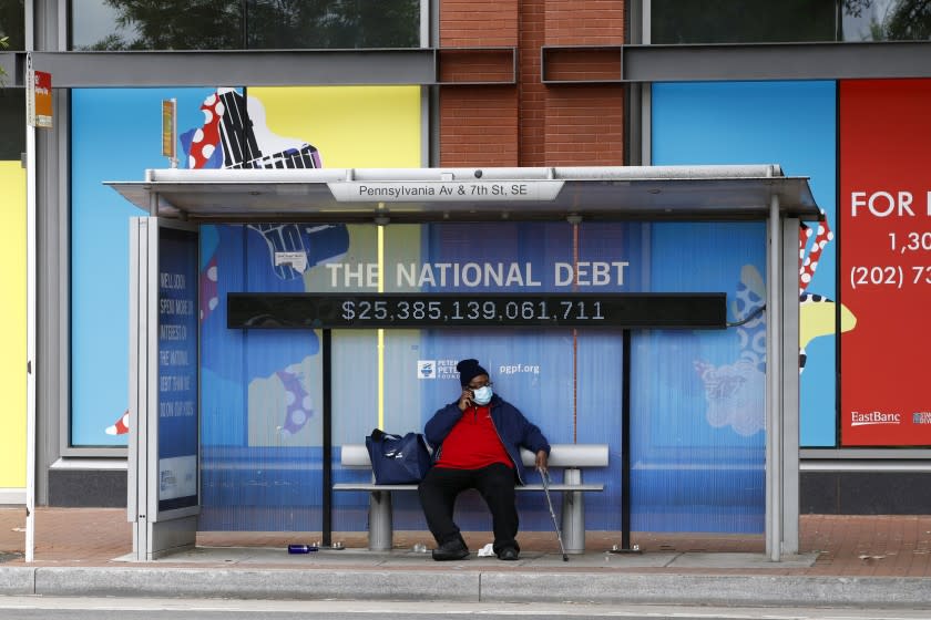 A man sits at a bus stop while wearing a face mask Thursday, May 21, 2020, in Washington. The District of Columbia is under a stay-home order for all residents in an effort to slow the spread of the new coronavirus. (AP Photo/Patrick Semansky)