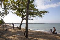 En esta imagen, tomada el 5 de abril de 2017, un jugador de béisbol se ejercita mientras empleados del Ministerio de Medio Ambiente limpian la playa Fray Antón de Montesinos, en Santo Domingo, República Dominicana. Según las estadísticas del gobierno, solo el 15% de quienes visitan República Dominicana pasan tiempo en Santo Domingo y solo el 3% duermen allí, atraídos por los paquetes de todo incluido en zonas costeras y desalentados por la falta de alojamientos de alto nivel en el casco histórico de la ciudad. (AP Foto/Tatiana Fernández)